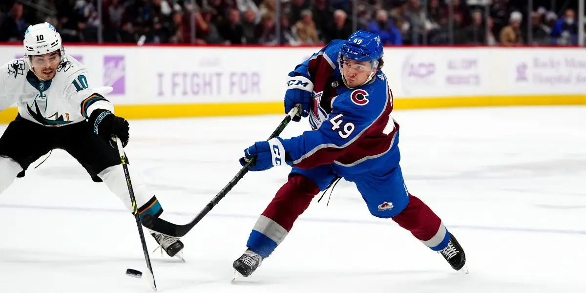 Samuel Girard taking a shot, while a San Jose Shark's skater attempts to check him with his stick