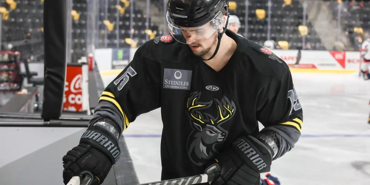 Iowa Heartlanders hockey player, Brendan Robbins is waxing his hockey stick that is leaning on the boards of the home bench.