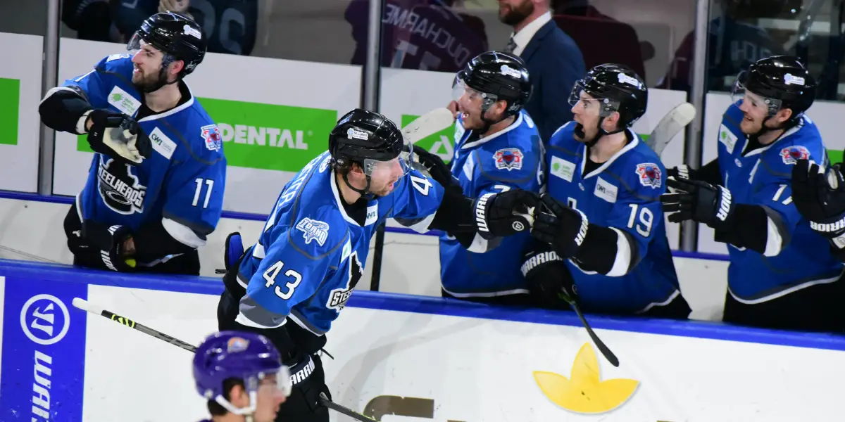An Idaho Steelhead hockey player skates to his bench after scoring a goal to celebrate with his teammates by giving fist bumps to the players on the bench.