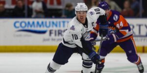 Jacksonville Icemen hockey player is skating towards the camera with the puck as a Solar Bears player follows behind over his left shoulder