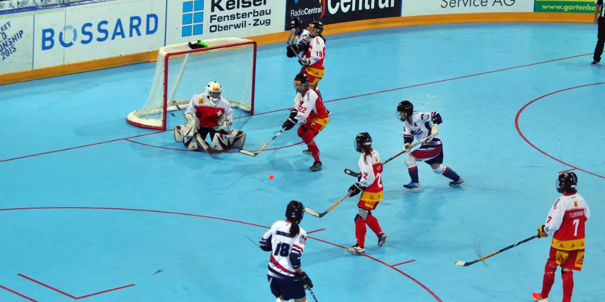 Six women playing ball hockey on a light blue floor.