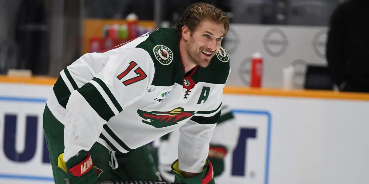 Marcus Foligno in a white Minnesota Wild jersey stretching on-ice before a game.